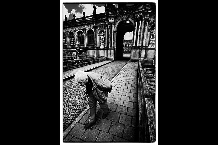 An old man walks hunched over away from the Zinger mit Semperbau in Dresden, Germany.