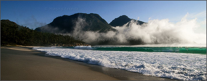 The fog lifts from Wine Glass Bay to reveal The Hazards in morning light — Freycinet National Park, Tasmania.