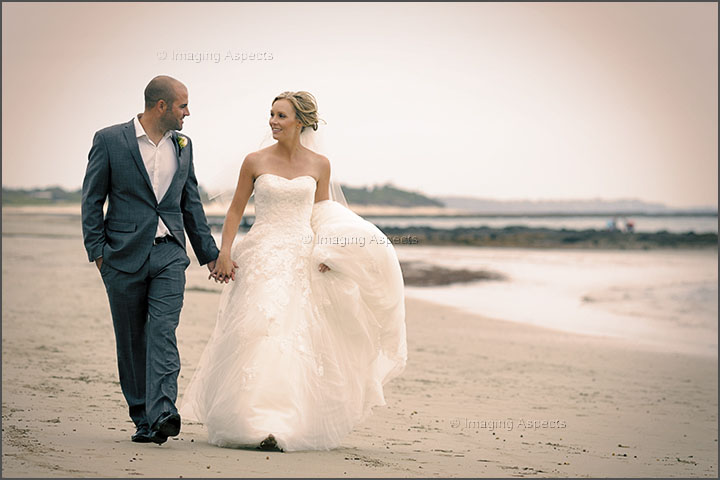 Newlyweds hold hands as they walk on the sand: Foreshore Reserve, Shoreham, Victoria.